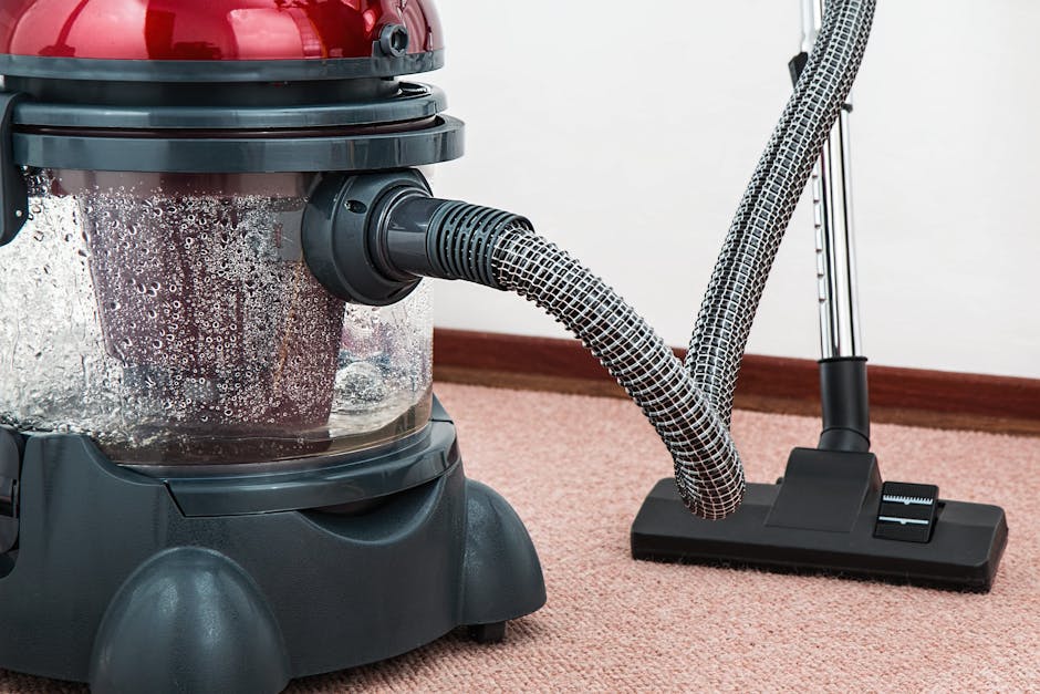 A woman using a yellow vacuum cleaner for surface cleaning and deep cleaning of a patterned rug with floral designs in a living room, featuring wooden flooring and a leather sofa. The room is well-lit